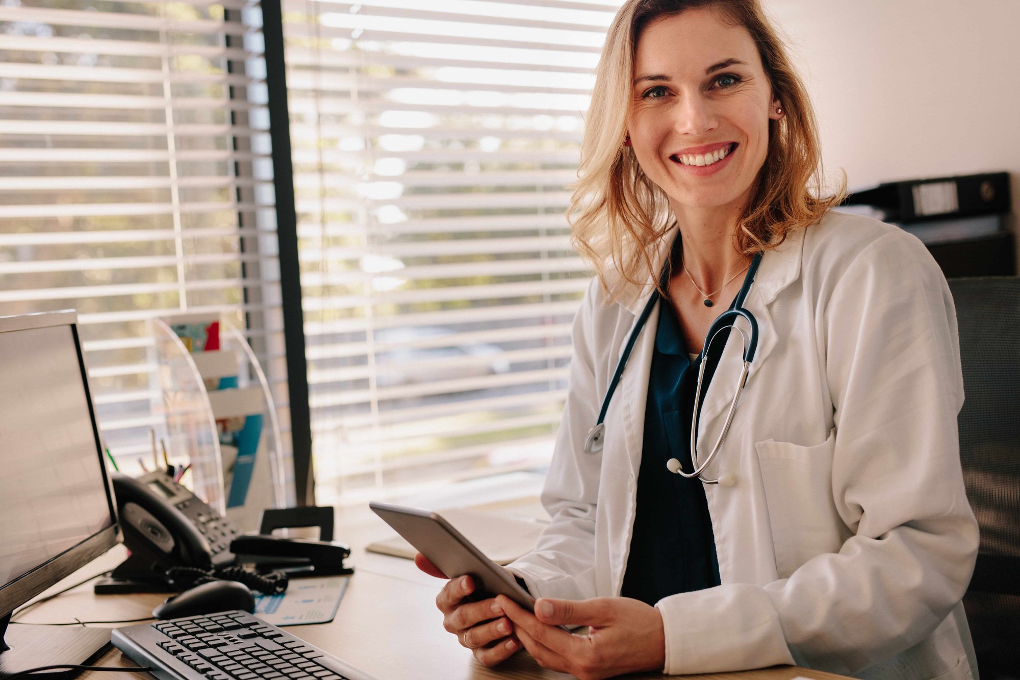 Friendly female doctor at her clinic desk_246365295-min